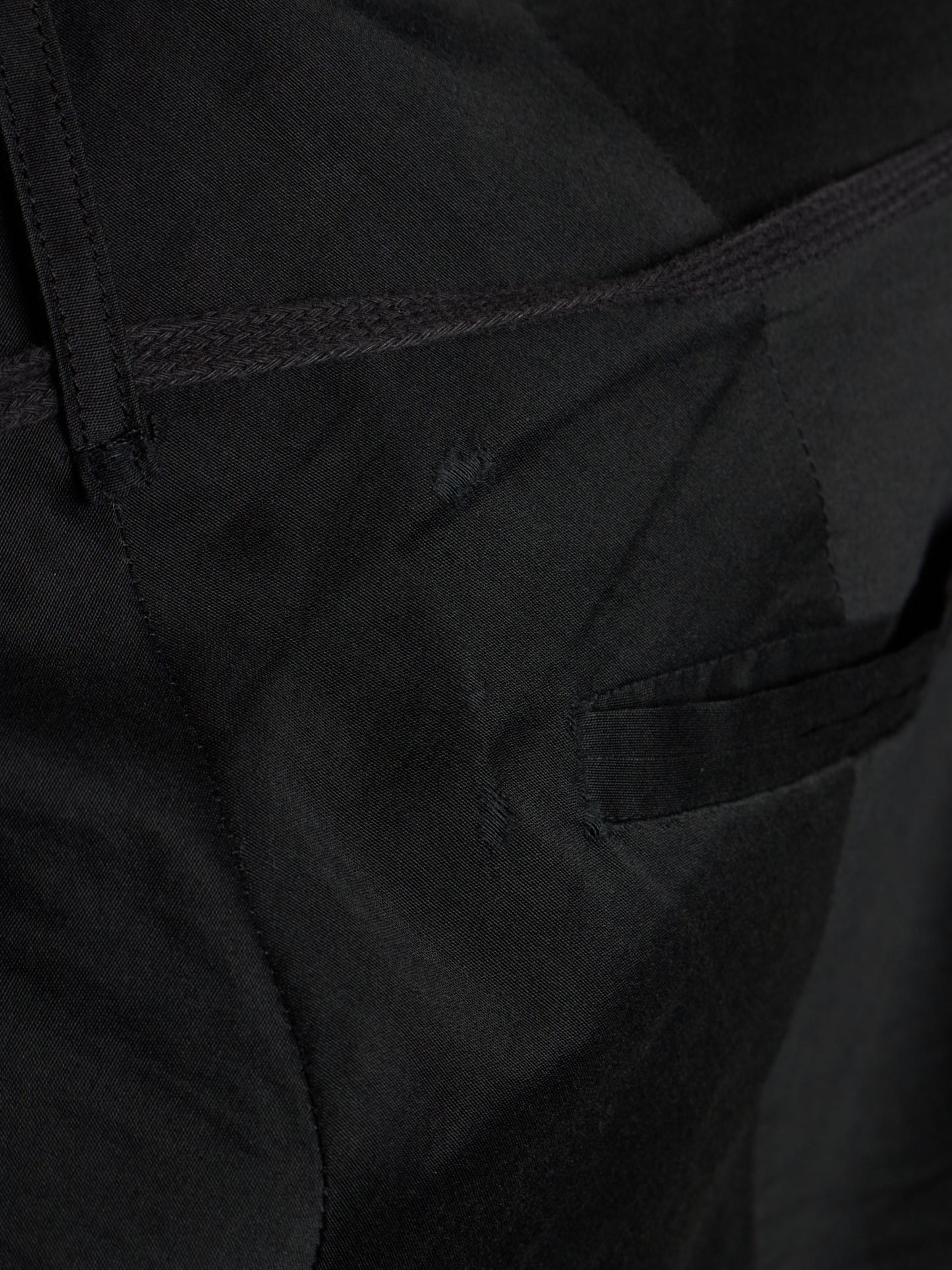Close-up detail shot of black fabric showing a side pocket seam, belt loop, and textured material.