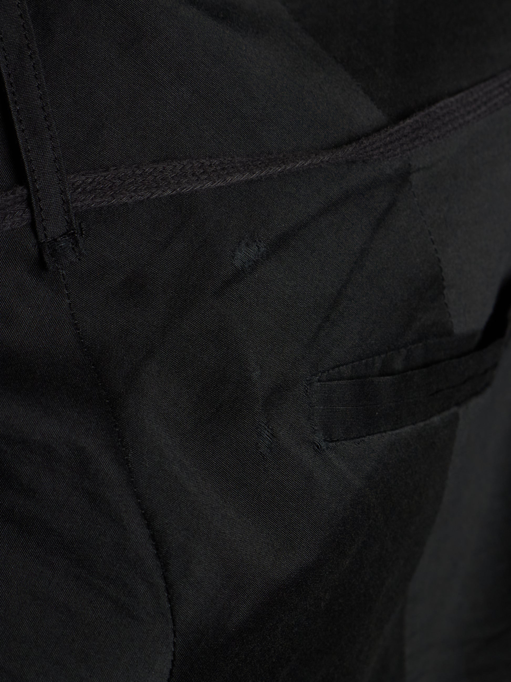 Close-up detail shot of black fabric showing a side pocket seam, belt loop, and textured material.