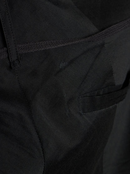 Close-up detail shot of black fabric showing a side pocket seam, belt loop, and textured material.