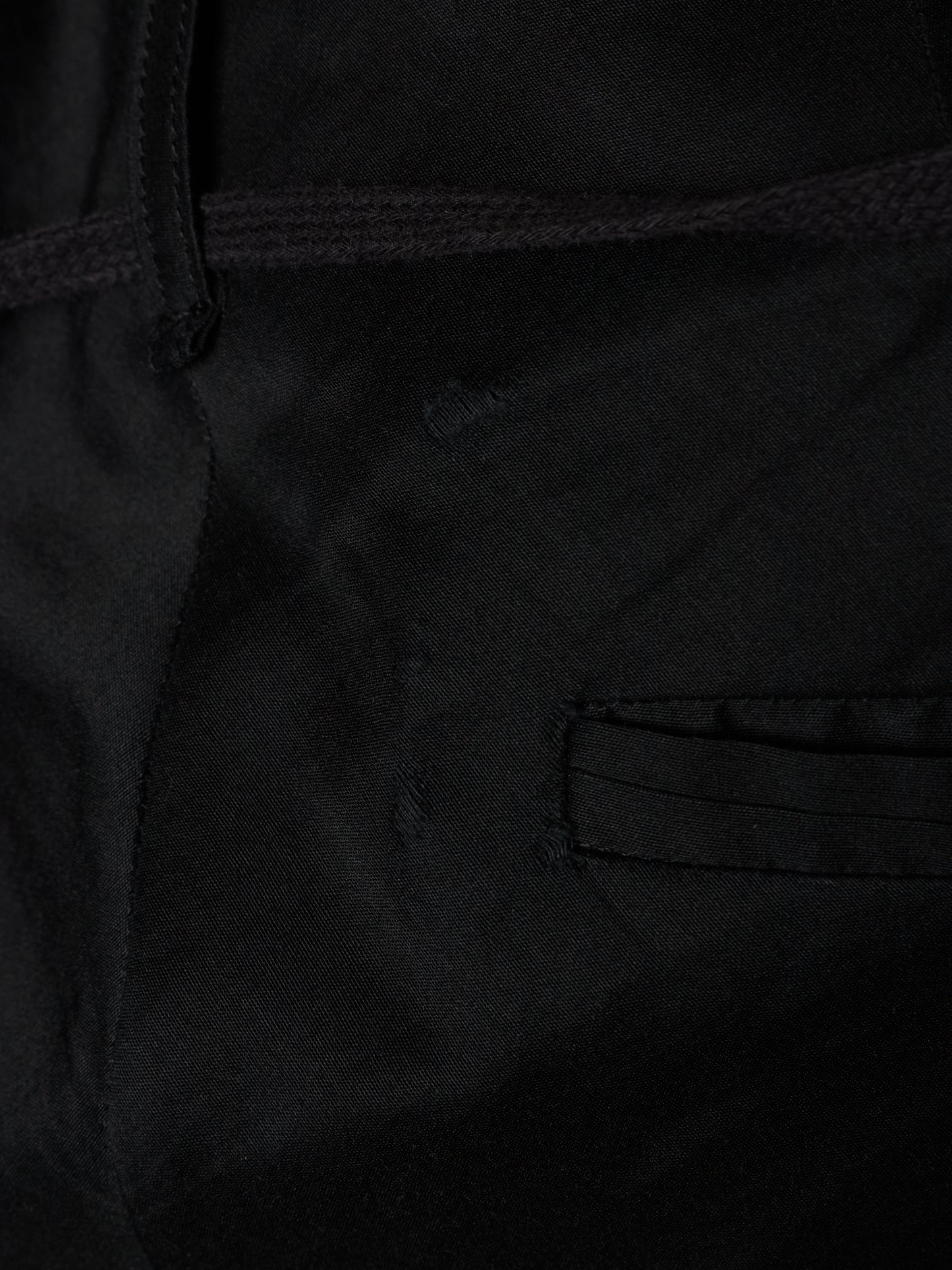 Close-up detail of a black fabric garment showing a stitched pocket and dark drawstring.