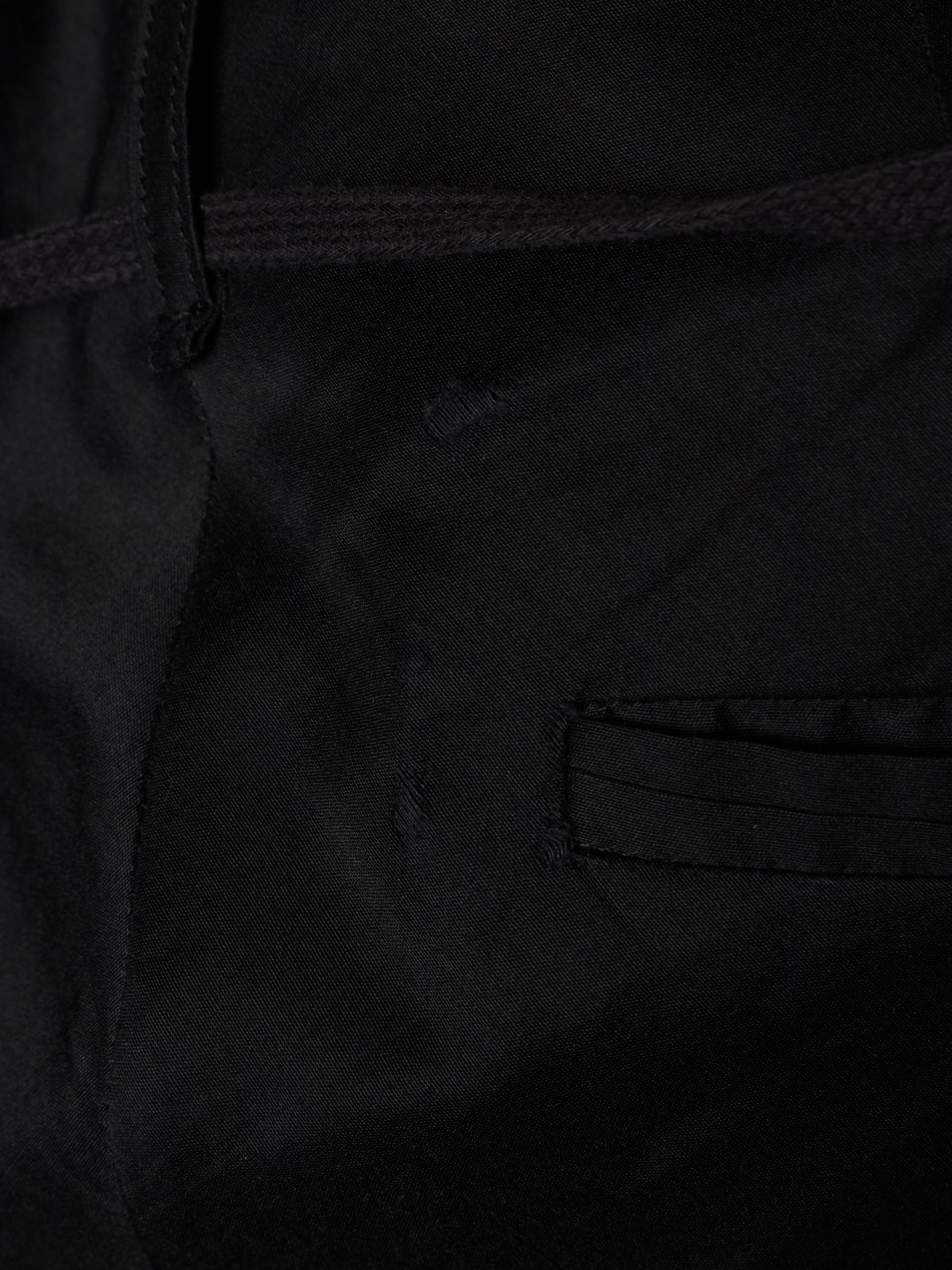 Close-up detail of a black fabric garment showing a stitched pocket and dark drawstring.
