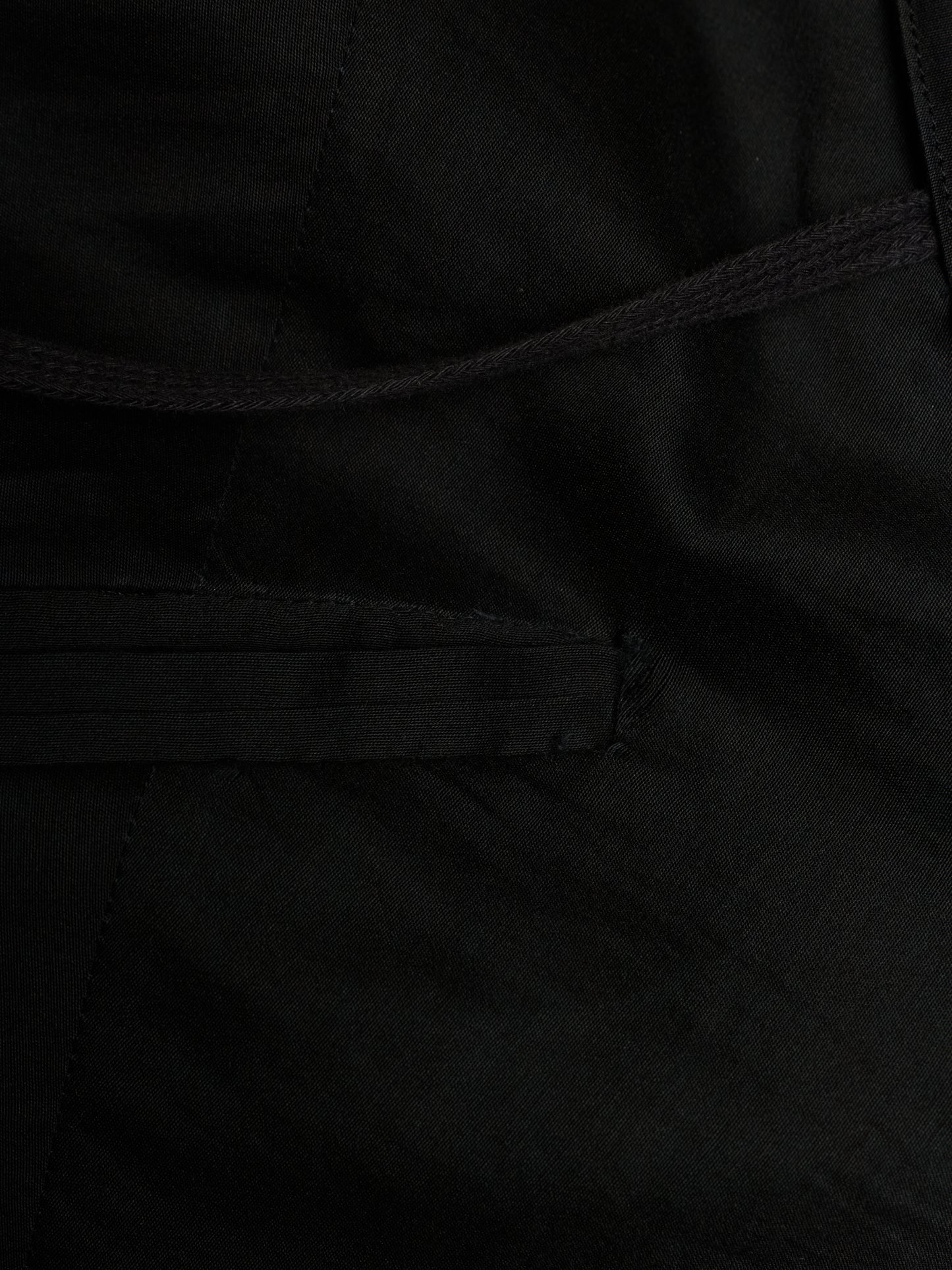 Close-up detail of a black fabric garment showing a stitched pocket and drawstring cord.