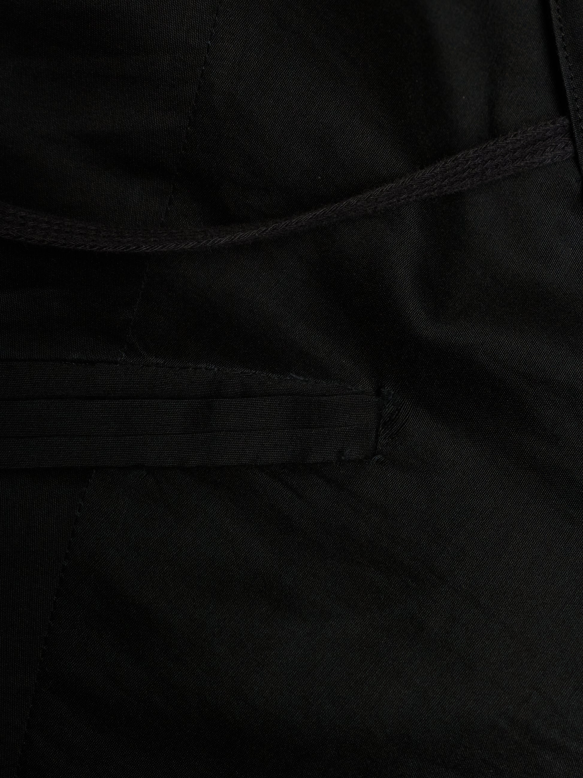 Close-up detail of a black fabric garment showing a stitched pocket and drawstring cord.