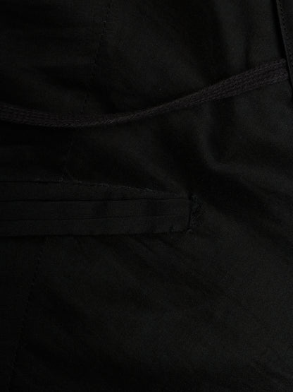 Close-up detail of a black fabric garment showing a stitched pocket and drawstring cord.