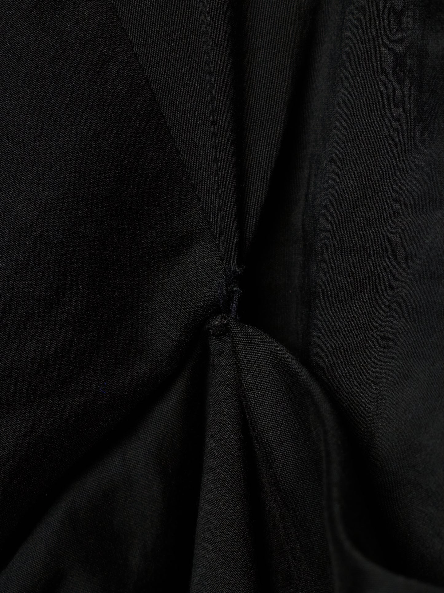 Close-up of a black fabric garment with gathered folds and a small button detail at the center.