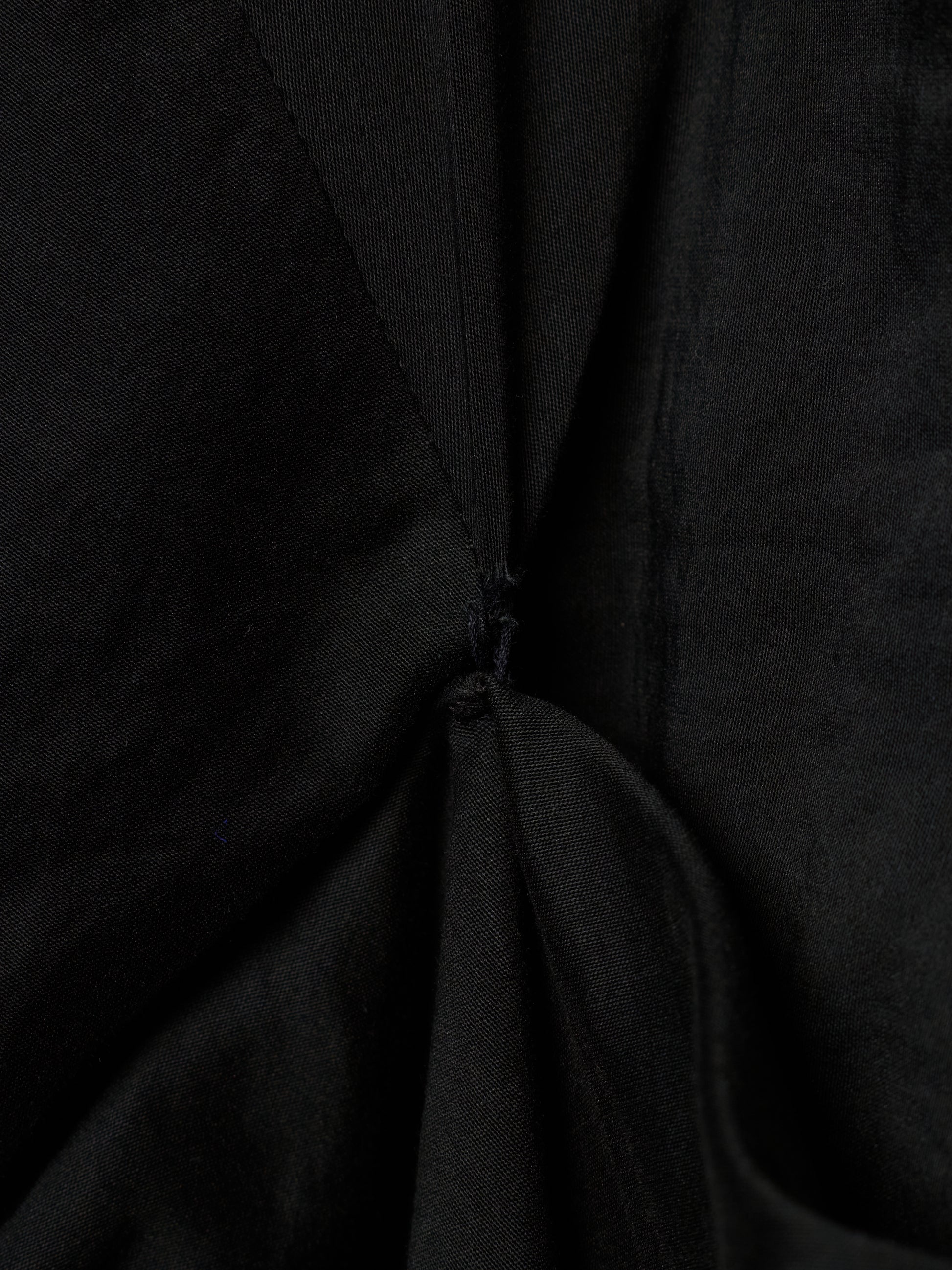 Close-up of a black fabric garment with gathered folds and a small button detail at the center.