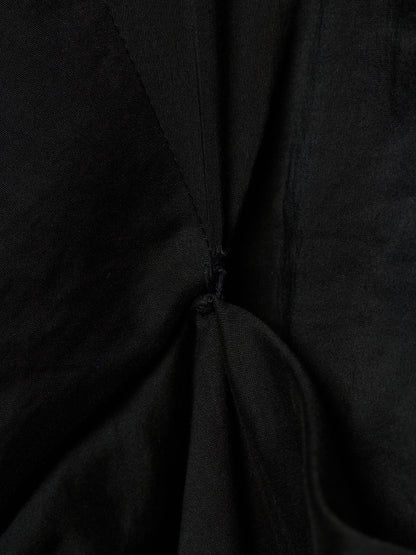Close-up of a black fabric garment with gathered folds and a small button detail at the center.