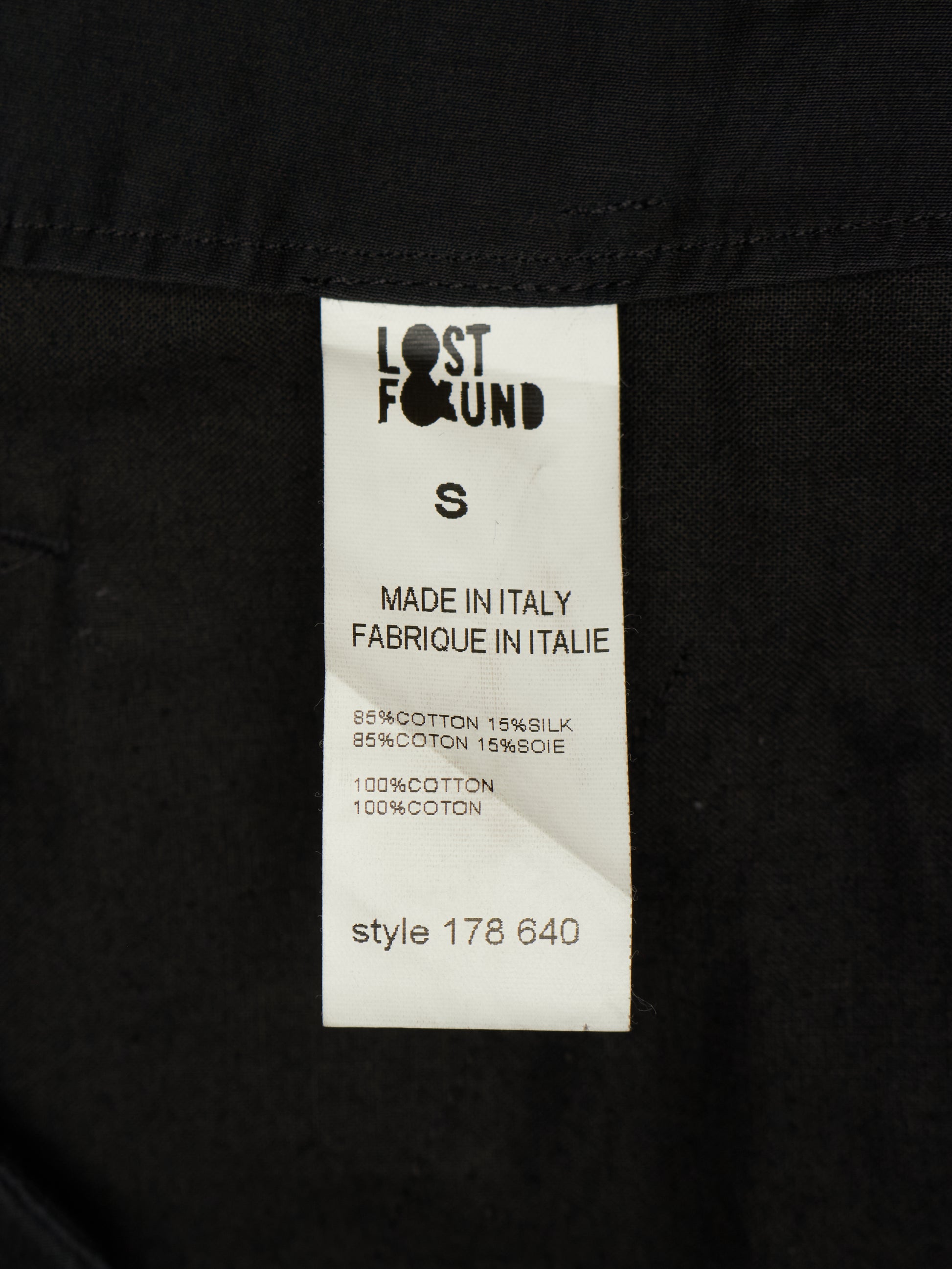 A close-up of a black garment's inner label, showing the Lost Found brand tag with size S and 'Made in Italy' text.