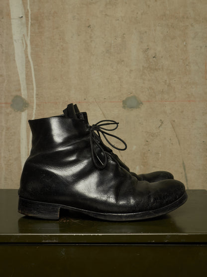 A pair of black leather lace-up ankle boots resting on a dark green surface against a textured beige wall.