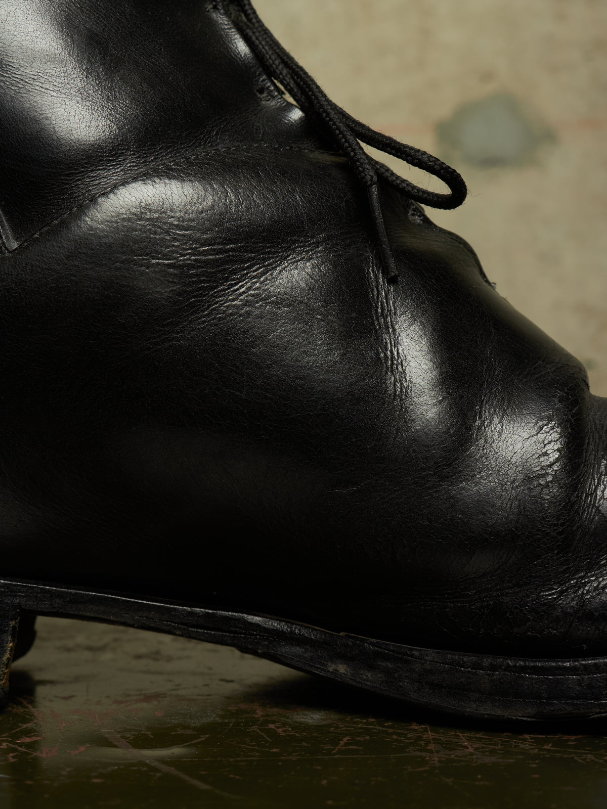A close-up of a black leather lace-up boot, showing the texture of the leather and the laces, set against a dark, moody background.