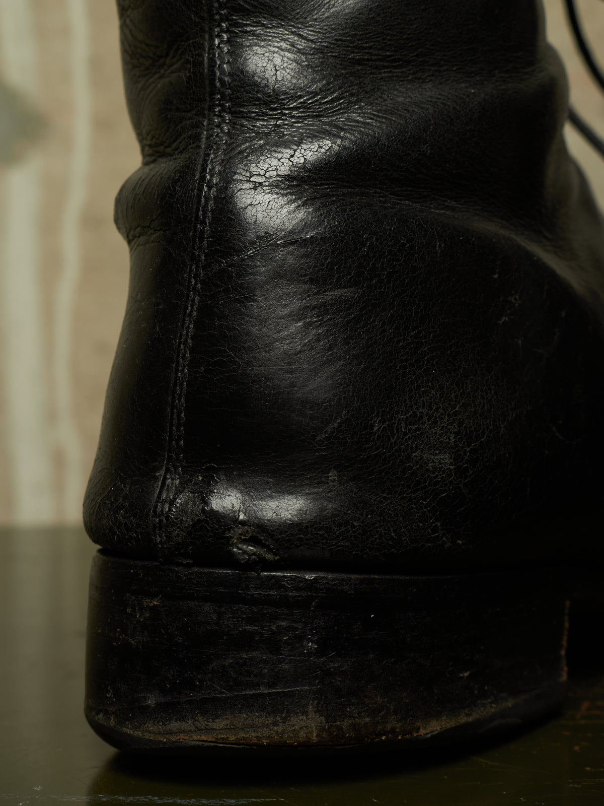Close-up of the heel and sole of a worn black leather boot, showing creasing, scuffing, and a worn outsole on a dark surface.