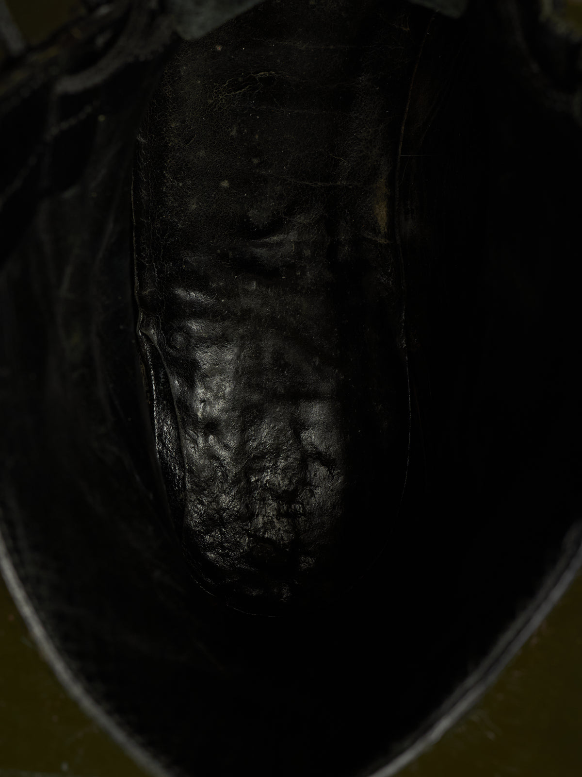 Close-up view inside the opening of a dark leather boot, showing the textured black leather footbed and a sliver of olive green outer material at the bottom.