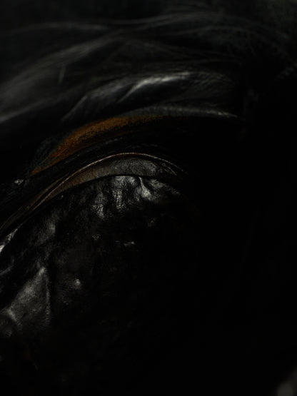 Close-up of a glossy black leather or faux-leather surface with dark hair or fibers across the top and a subtle warm brown accent visible in the light.