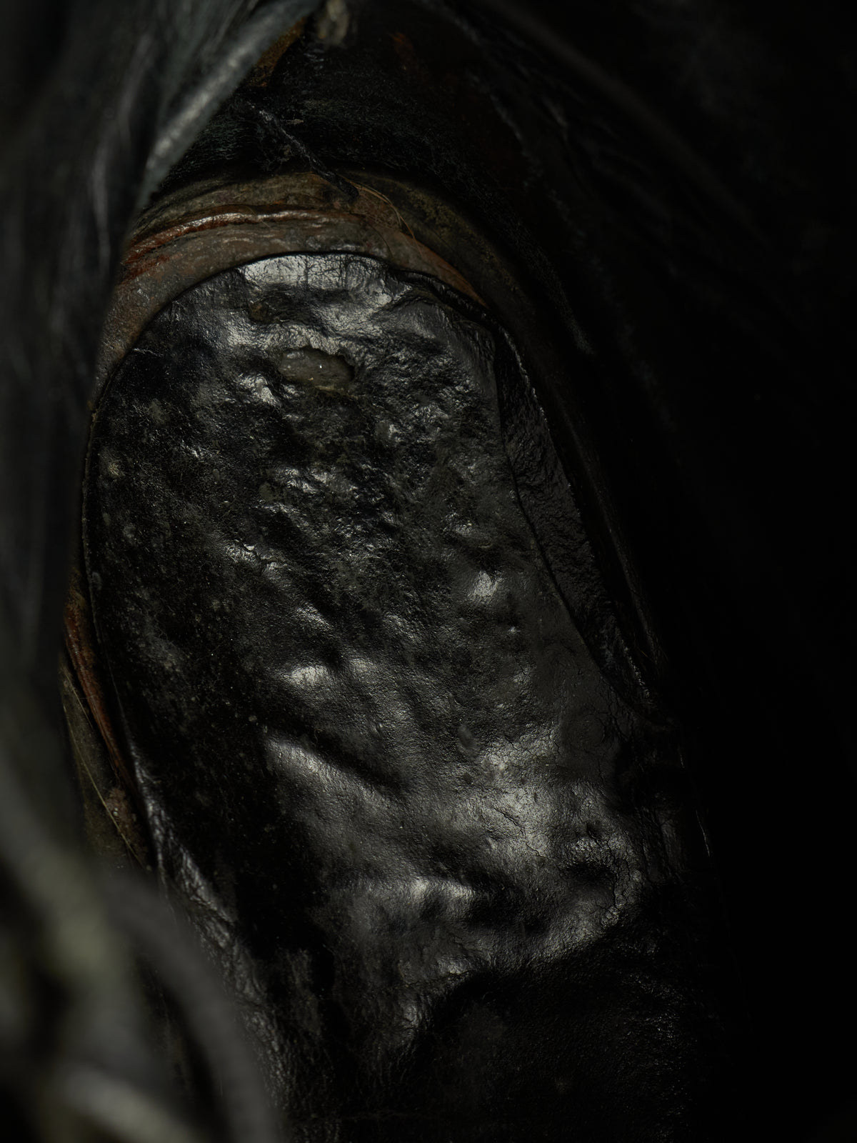 A close-up view of a dark, textured black leather boot or shoe interior with a glossy, reflective surface.