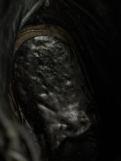 A close-up view of a dark, textured black leather boot or shoe interior with a glossy, reflective surface.