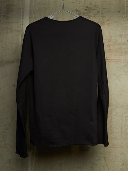 A black long-sleeve crewneck shirt hanging on a clear plastic hanger against a textured concrete wall.
