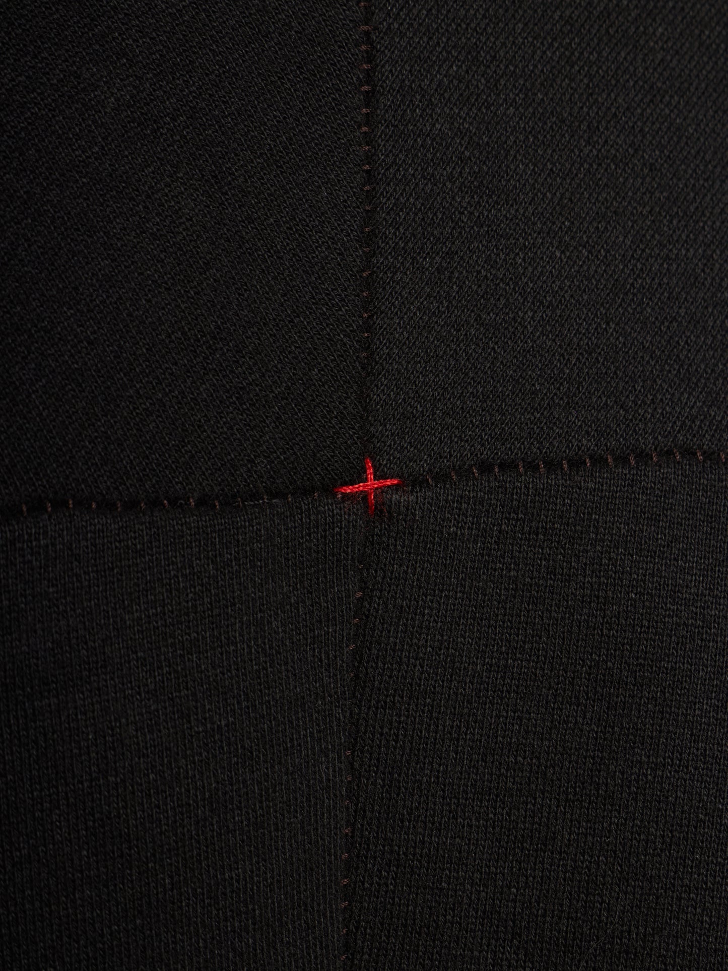 Close-up of a black ribbed knit fabric with a small red stitched cross mark at the center seam intersection.