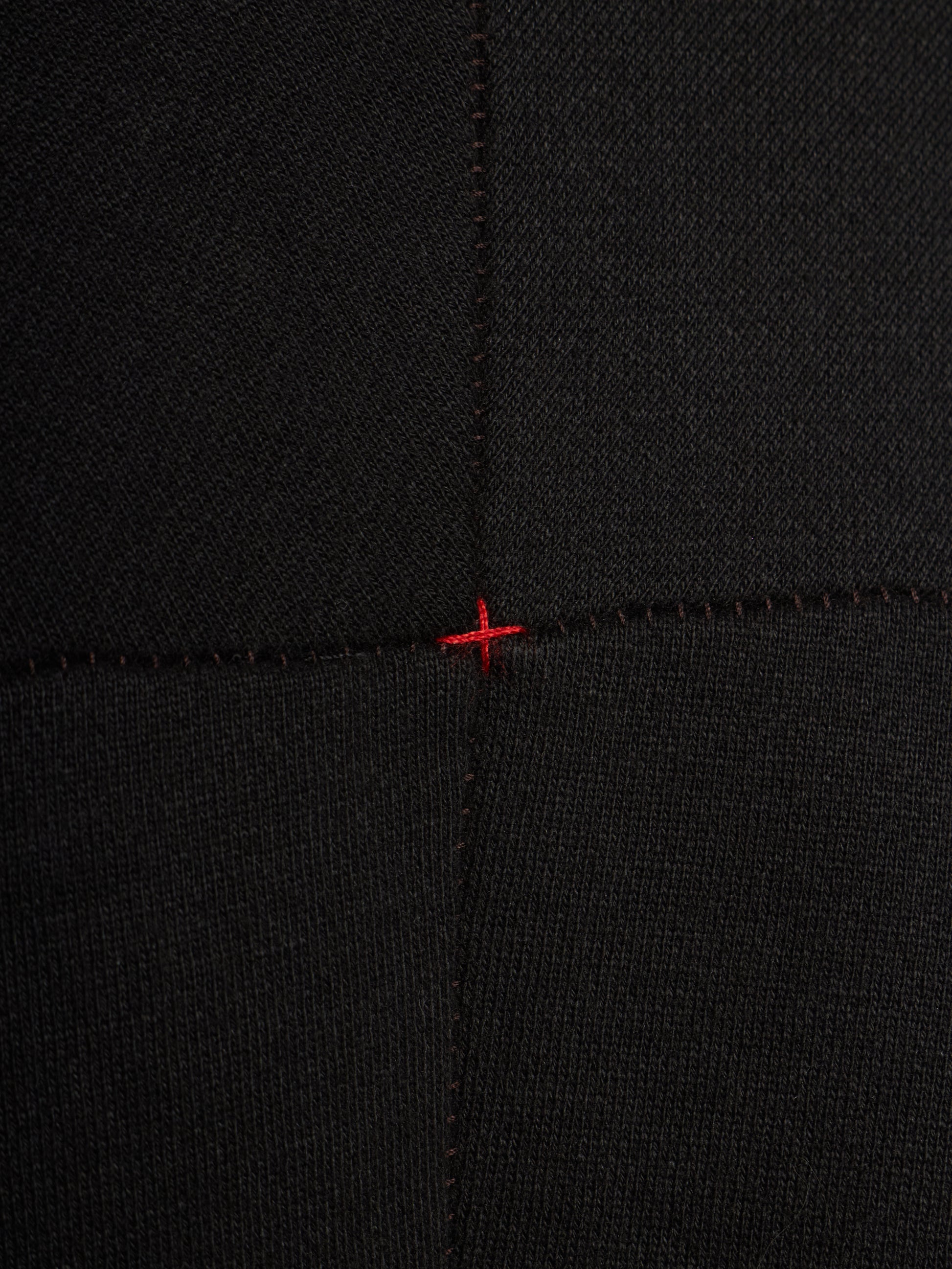 Close-up of a black ribbed knit fabric with a small red stitched cross mark at the center seam intersection.