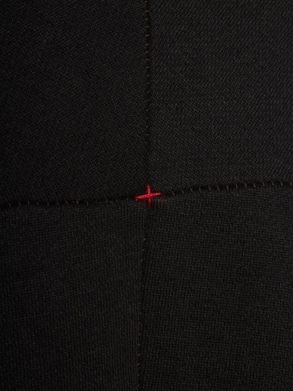 Close-up of a black ribbed knit fabric with a small red stitched cross mark at the center seam intersection.