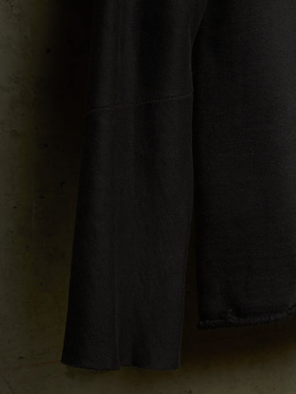 Close-up of a dark charcoal gray fabric garment, showing a seam and a raw, frayed hem against a textured, warm-toned background.