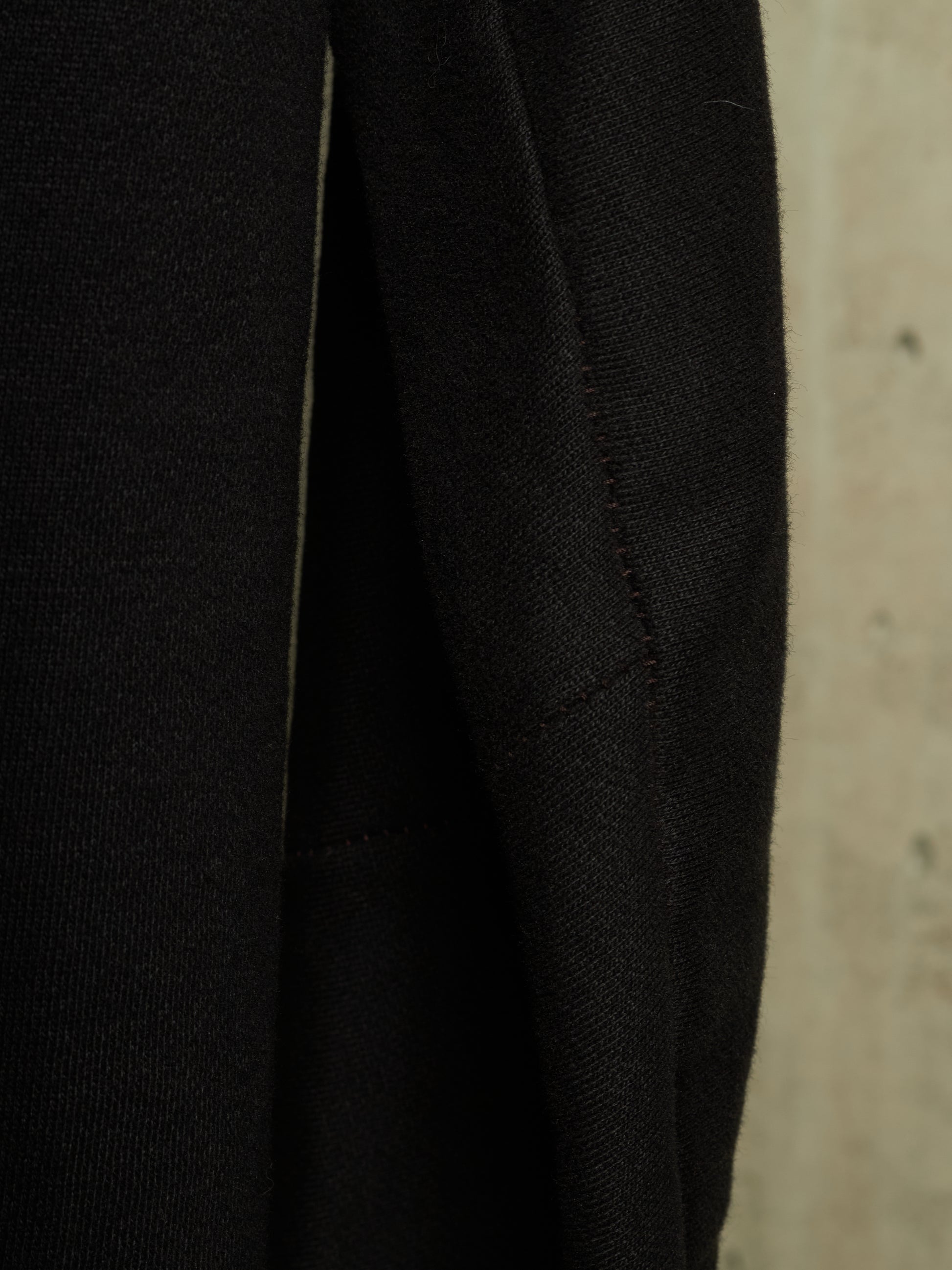 Close-up detail of a black textured fabric garment, showing a seam and weave against a neutral beige background.