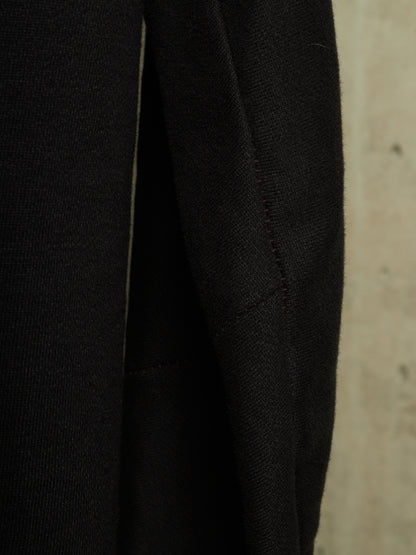 Close-up detail of a black textured fabric garment, showing a seam and weave against a neutral beige background.