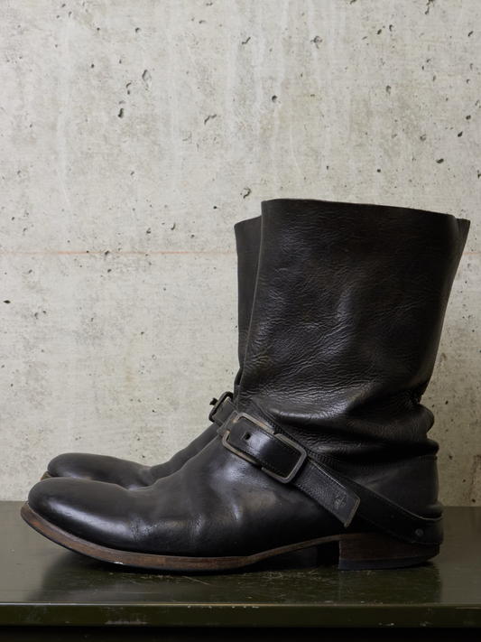 Pair of black leather boots with buckles on a concrete surface