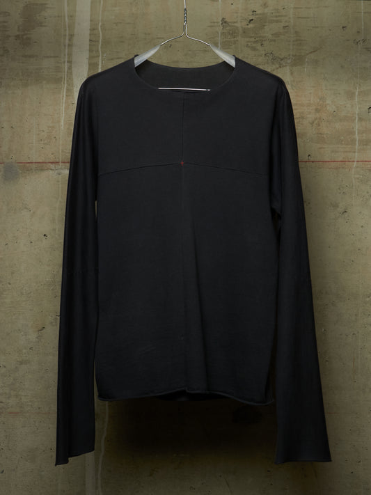 A black long-sleeve crewneck top hanging on a white hanger against a textured concrete wall.