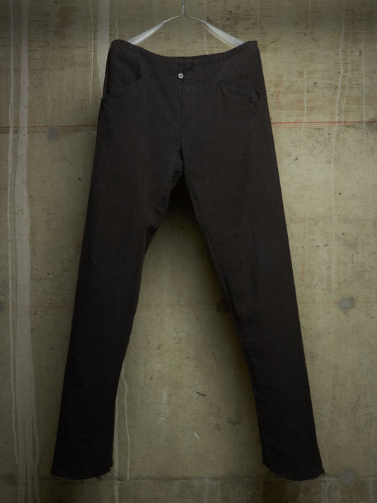 Dark brown slim-fit pants hanging on a white plastic hanger against a textured concrete wall.