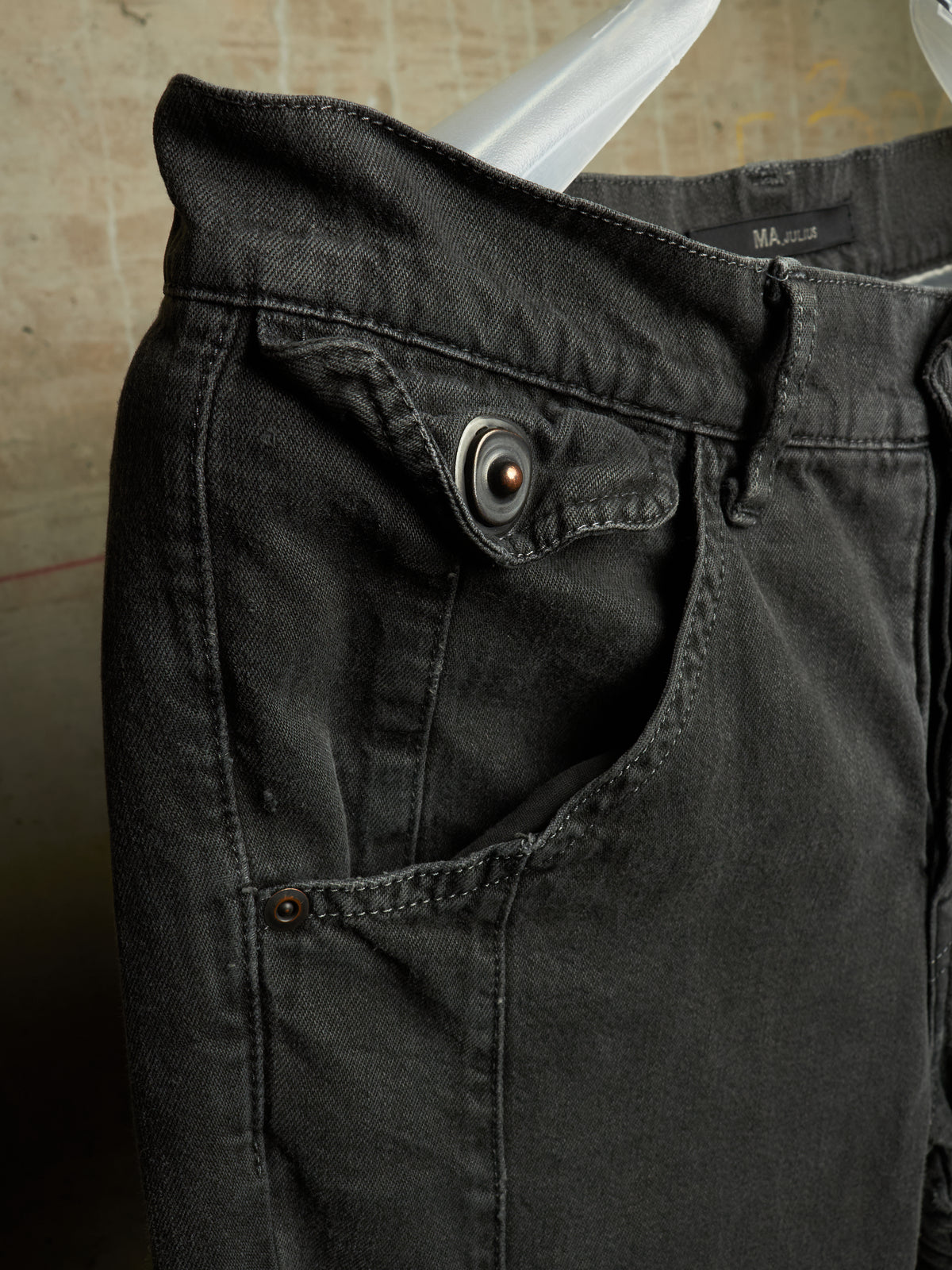 Close-up of a pair of dark charcoal gray denim jeans hanging on a white plastic hanger against a textured beige wall. The photo highlights the waistband, buttoned pocket, and fabric texture.