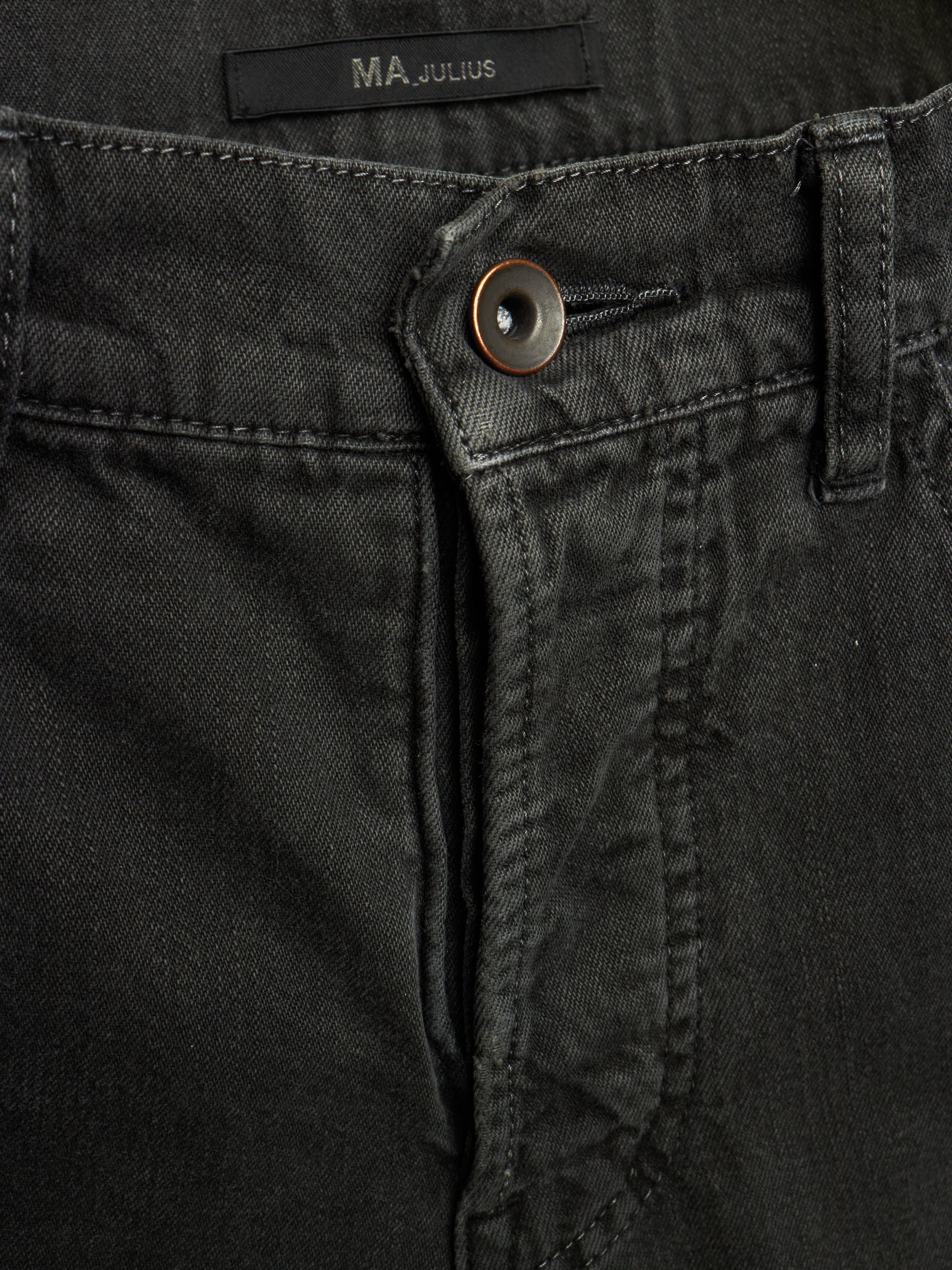 Close-up of black denim jeans showing the button closure, belt loop, and waistband label with the brand name MA JULIUS.
