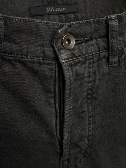 Close-up of black denim jeans showing the button closure, belt loop, and waistband label with the brand name MA JULIUS.