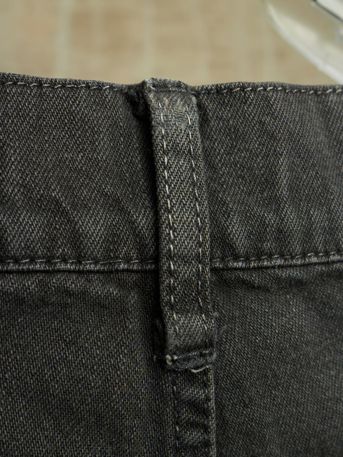 Close-up detail of a pair of dark gray or black denim shorts showing the waistband, belt loop, and stitching.