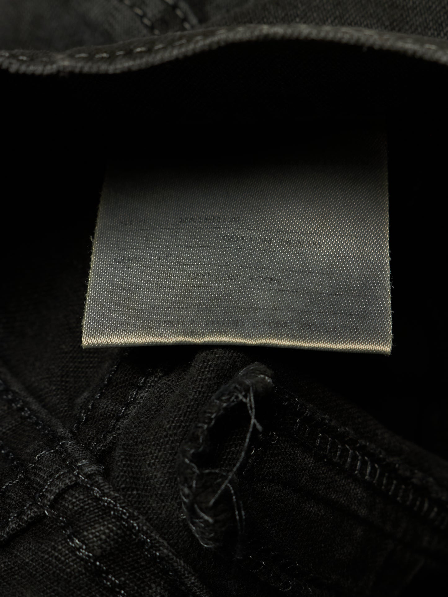 Close-up of the inside waistband of black denim jeans, showing a sewn-on fabric size and material label.