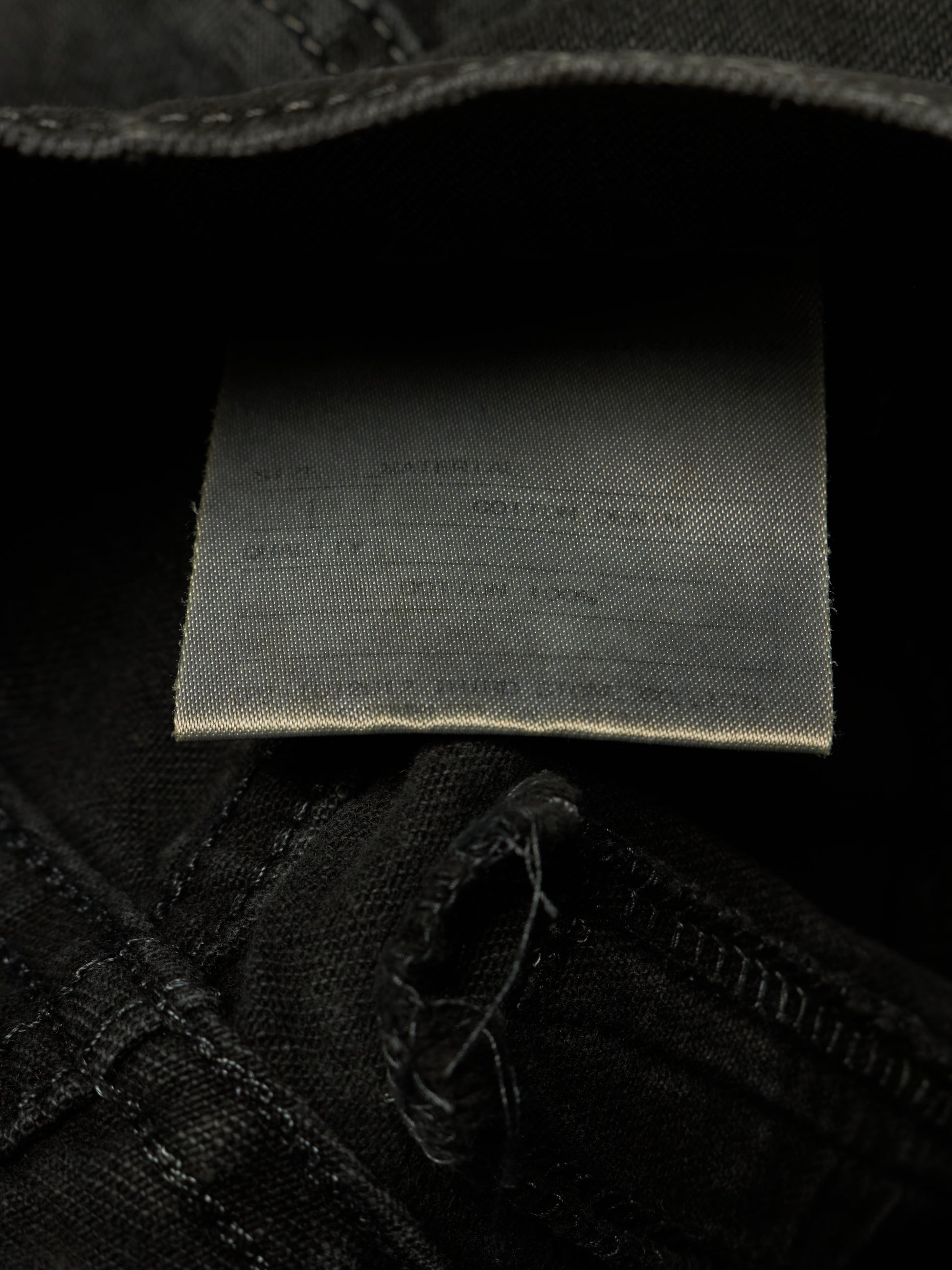Close-up of the inside waistband of black denim jeans, showing a sewn-on fabric size and material label.