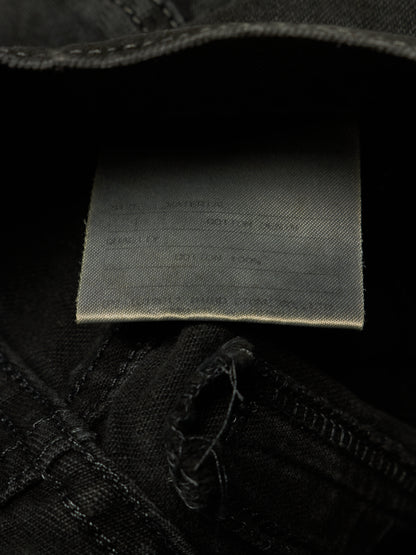 Close-up of the inside waistband of black denim jeans, showing a sewn-on fabric size and material label.