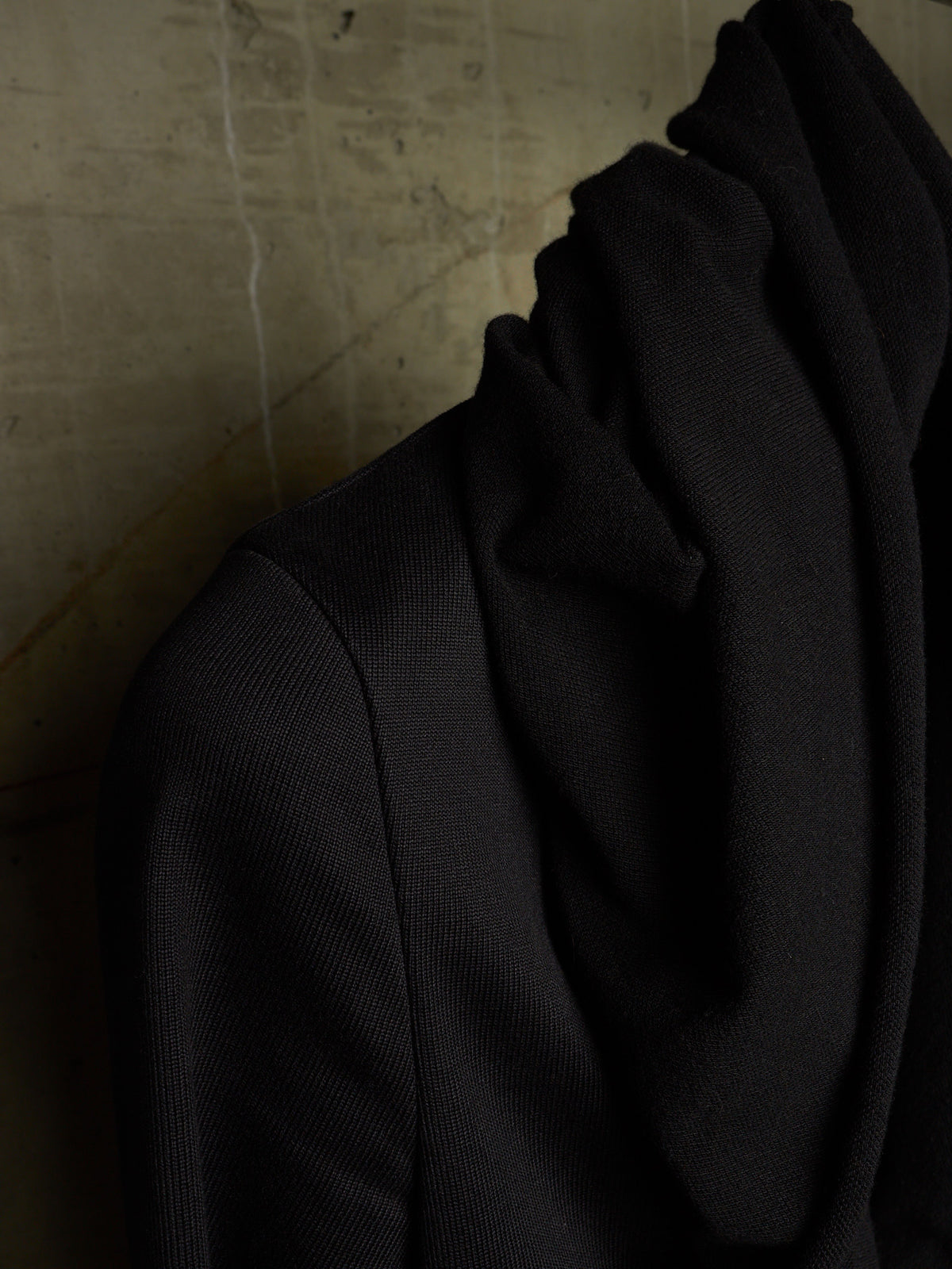 A close-up of a black ribbed knit garment draped against a textured beige wall.