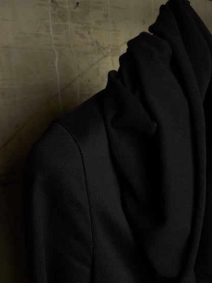 A close-up of a black ribbed knit garment draped against a textured beige wall.