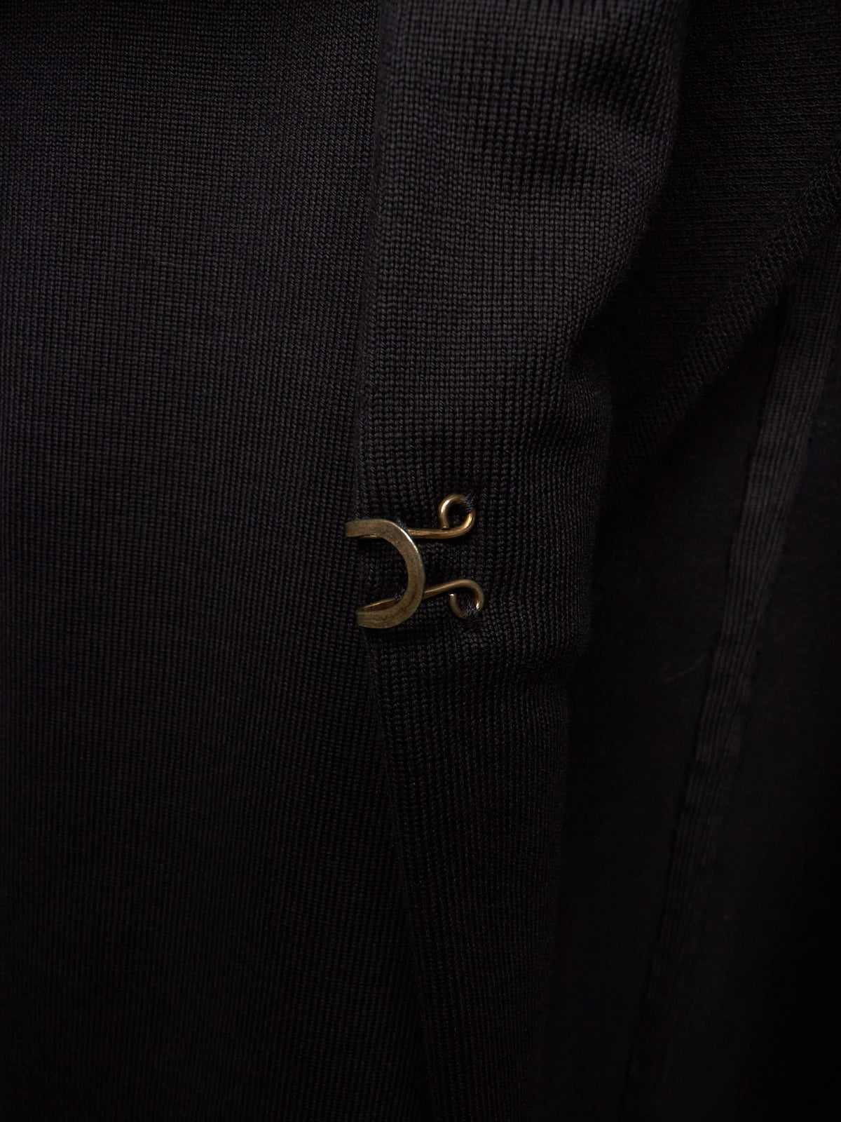 Close-up of a black ribbed fabric garment featuring a small metallic gold crescent moon and scroll emblem on the chest.