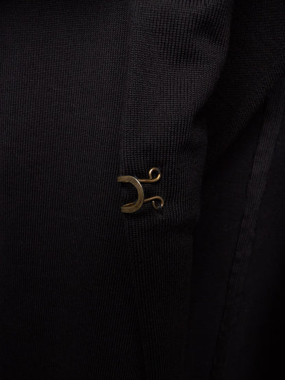 Close-up of a black ribbed fabric garment featuring a small metallic gold crescent moon and scroll emblem on the chest.
