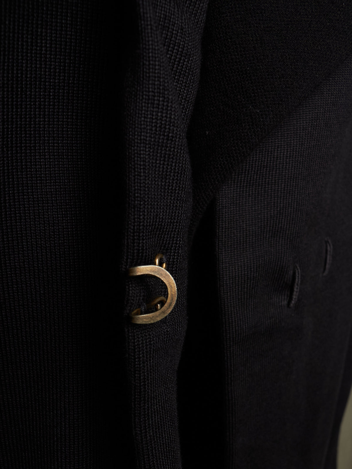 Close-up of a black textured knit garment featuring a prominent gold-tone metal D-ring detail on the front.