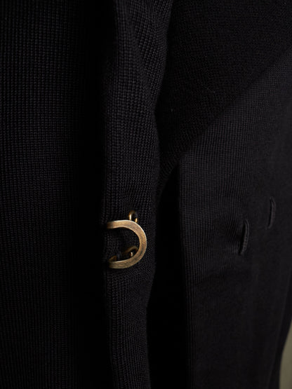 Close-up of a black textured knit garment featuring a prominent gold-tone metal D-ring detail on the front.