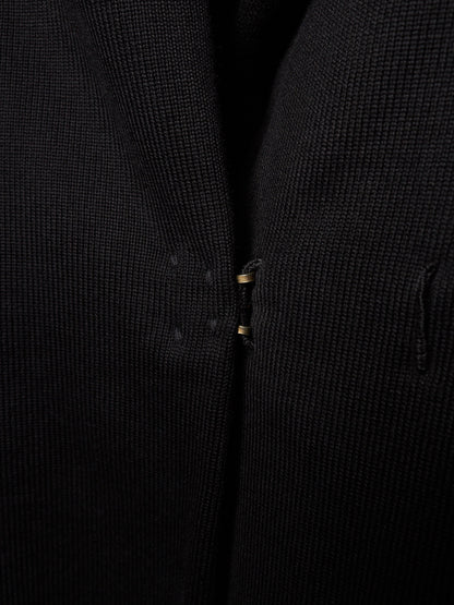 Close-up of a black textured knit garment, showing the fine ribbed fabric and a small gold-toned zipper pull.