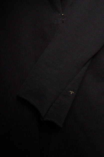 Close-up of a black ribbed knit garment, showing the texture of the fabric and a small gold embroidered logo on the cuff.