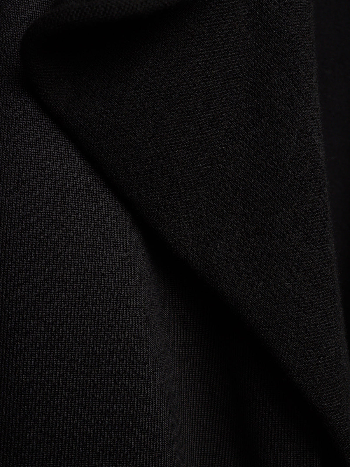 A close-up of black textured fabric with soft folds and a fine woven surface.