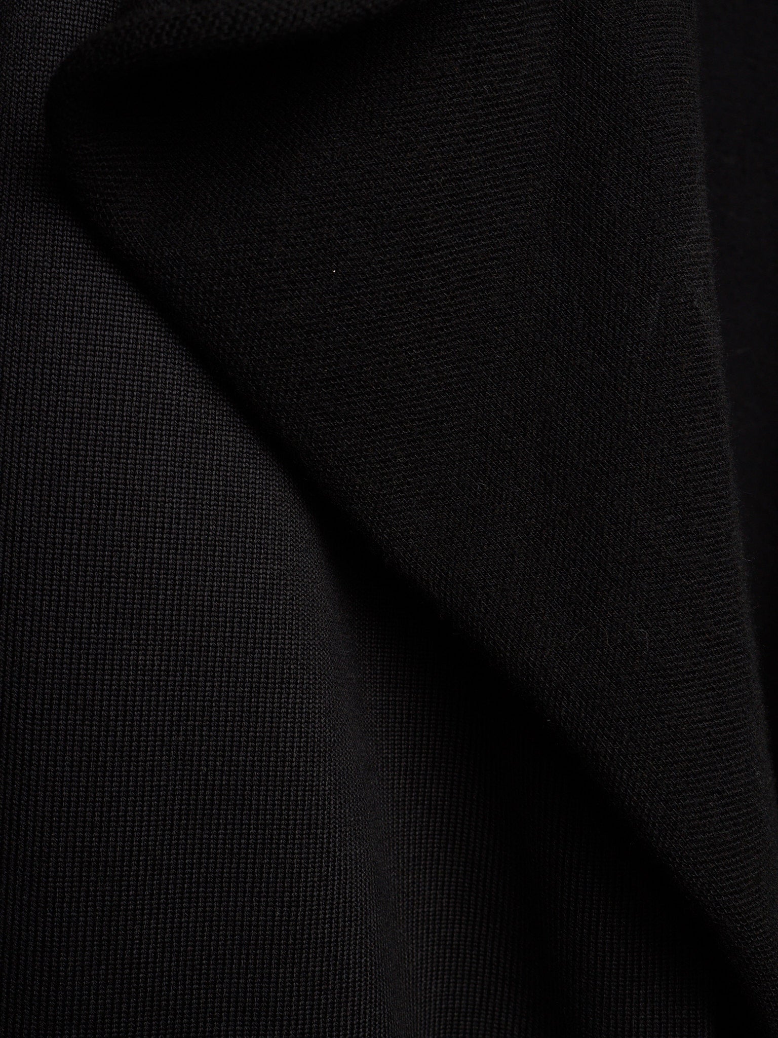 A close-up of black textured fabric with soft folds and a fine woven surface.