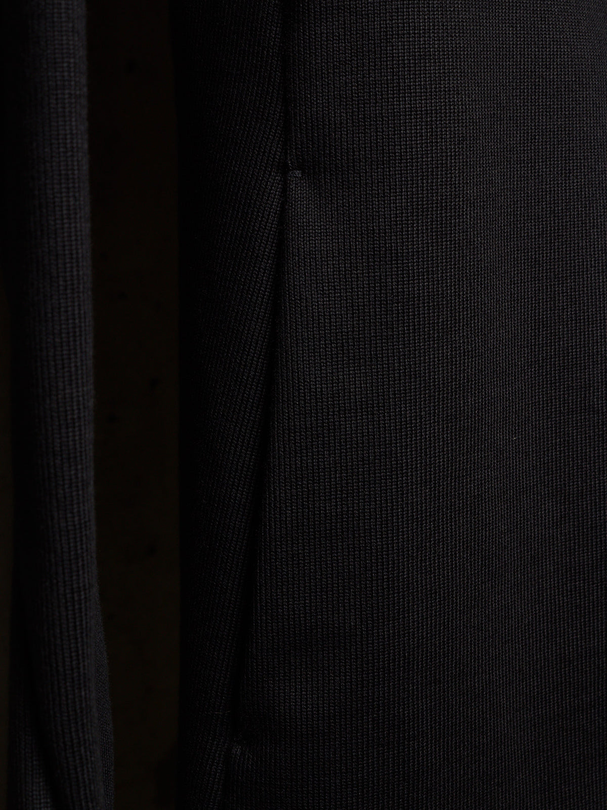 Close-up of a dark ribbed knit fabric with a fine vertical texture and a subtle seam running down the center.