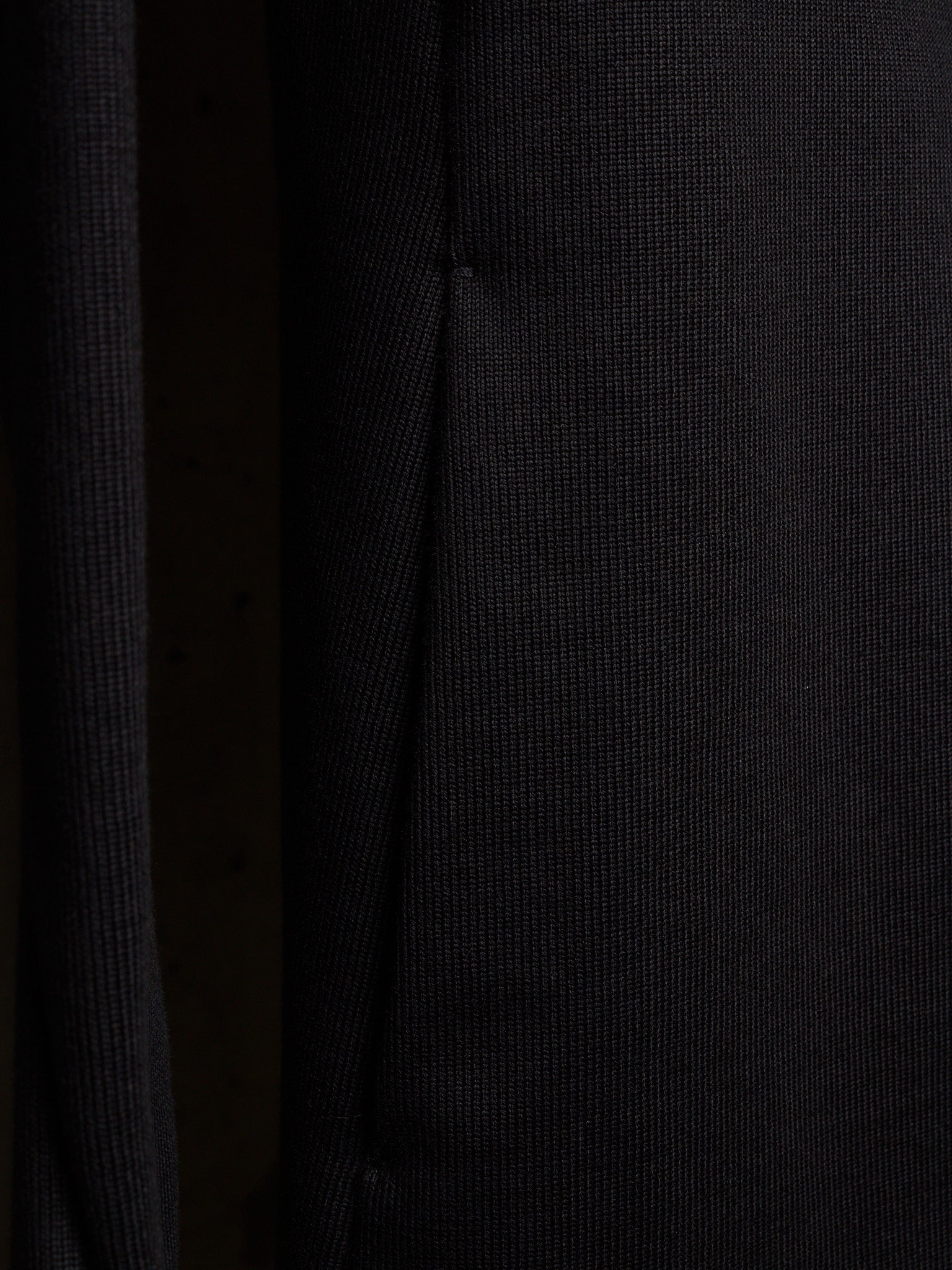 Close-up of a dark ribbed knit fabric with a fine vertical texture and a subtle seam running down the center.