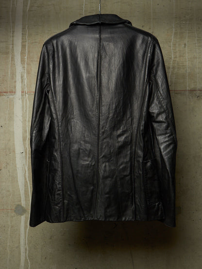 A black leather jacket hanging against a textured concrete wall, showing the back view with a central seam and collar.
