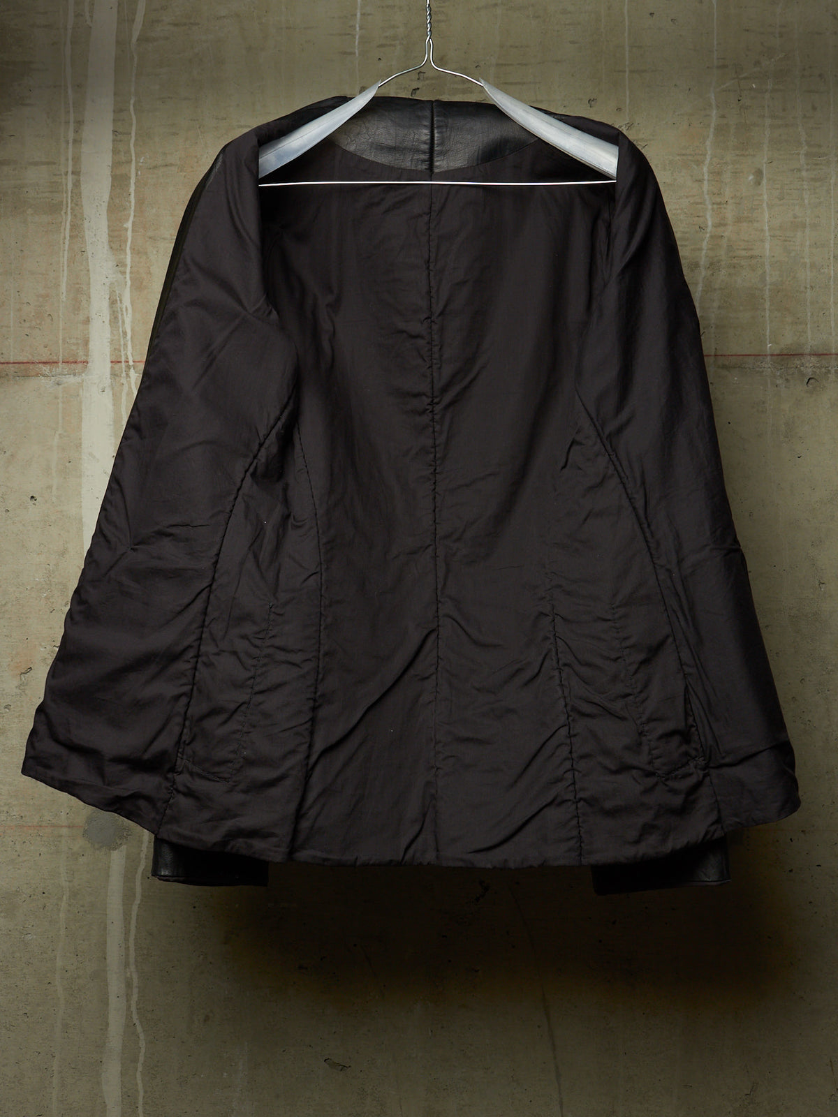 A dark brown quilted jacket hanging on a white hanger against a textured concrete wall.